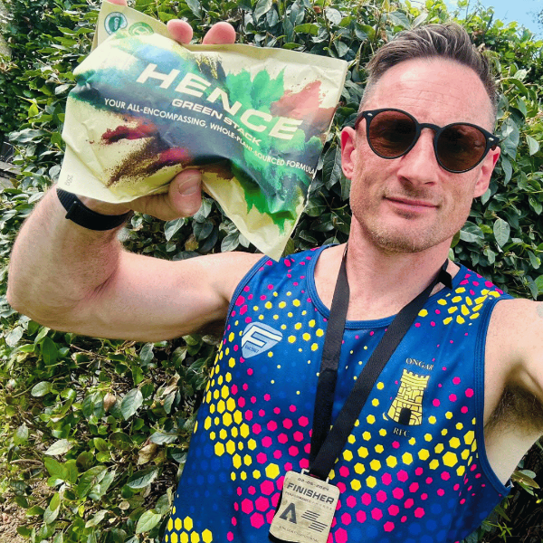 Runner holding Hence Greens pouch after race — wearing finisher medal and athletic vest