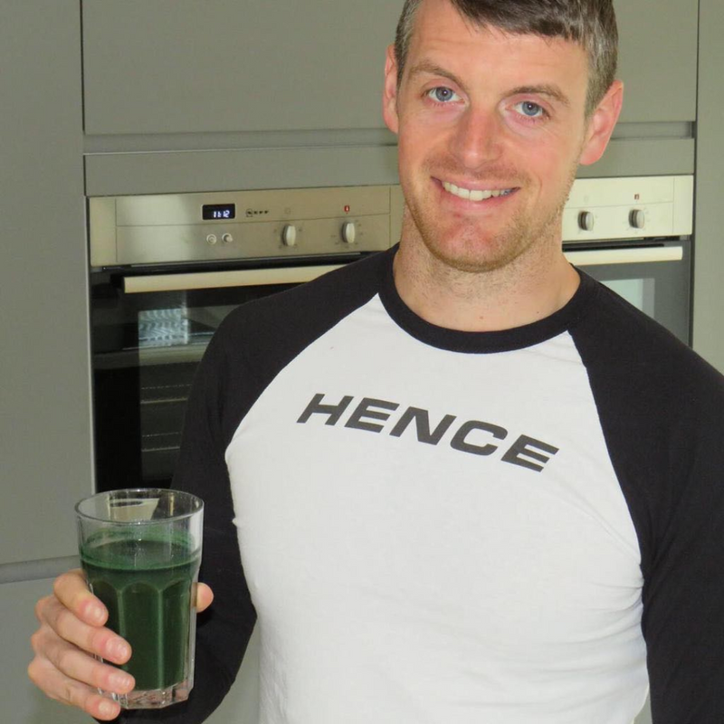 Hence founder wearing branded t-shirt, holding a freshly mixed glass of Hence Greens in kitchen